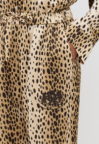 Set de pijamale din satin cu imprimeu leopard, caracterizat printr-un elastic la talie, detaliu cu fundiță și o broderie cu logo negru pe lateral.