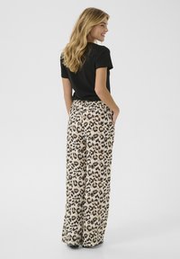 Chemise noire à manches courtes associée à un pantalon taille haute à jambes larges avec un motif léopard beige et marron, doté de poches.