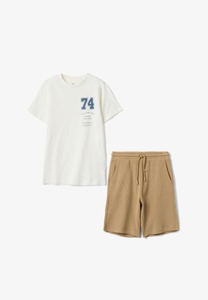 Weißes T-Shirt mit kurzen Ärmeln, blauem "74"-Aufdruck und kursivem Text, kombiniert mit hellbraunen Shorts mit Kordelzug und Fronttaschen.