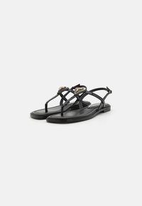 Zwarte platte sandalen met een T-band ontwerp, voorzien van gouden hardware-accents en een gladde leerachtige textuur. Dunne banden en een minimalistisch profiel.