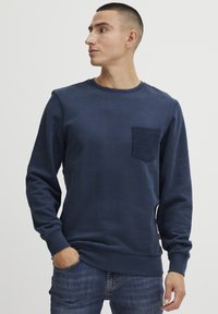 Felpa blu navy in cotone, con taschino a patch testurizzato, scollo rotondo e polsini e orlo a coste. Il modello la indossa con dei jeans.