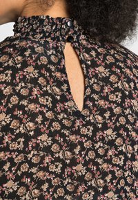 Blusa floreale con fondo nero decorato da piccoli motivi di fiori beige e rossi, colletto alto arricciato e spacco posteriore con bottoni.