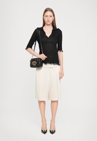 Top preto de malha com decote em V e mangas curtas, calções plissados em creme, mala preta com logótipo dourado, e sapatos de salto agulha pretos.