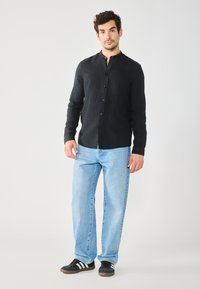Camisa negra de botones con cuello mao, combinada con jeans rectos de color azul claro y zapatillas negras con rayas blancas.