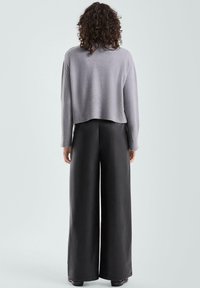 Szary krótki sweter o teksturowanym splocie zestawiony z czarnymi spodniami o szerokich nogawkach; gładki materiał i prosty design. Brak widocznych metalowych elementów czy ozdób.