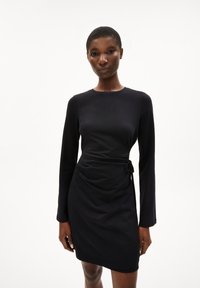 Zwarte jurk met lange mouwen en een aansluitend silhouet, voorzien van een taille met strikdetail en een gladde textuur, ideaal voor casual of formele gelegenheden.