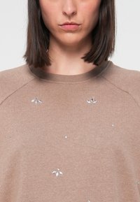 Sweatshirt marron à col rond, orné de strass argentés disposés en fleurs et confectionné dans un tissu doux et texturé.