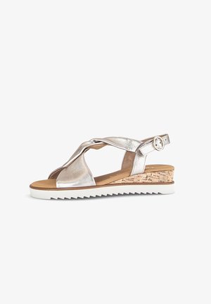 Sandales à talon compensé en cuir argenté avec des brides croisées, semelle en liège et semelle en caoutchouc blanche. Dispose d'une sangle de cheville ajustable avec boucle.