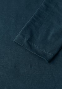 Szmaragdowa koszula z długim rękawem, uszyta z miękkiej, fakturowanej tkaniny. Posiada okrągły dekolt oraz kontrastowe przeszycia wzdłuż rękawów.