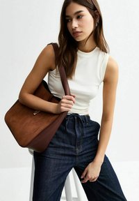 Sac à main en faux daim marron avec une finition texturée, doté d'une bandoulière lisse et d'un simple accent métallique, associé à un denim foncé.