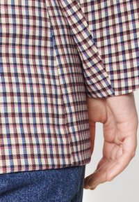 Knapp-up skjorta med ett flerfärgat rutmönster i röd, blå och svart på en vit bakgrund; har en rundad nederkant och uppvikta ärmar.