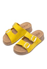 Sandales à glissière en daim jaune avec deux boucles réglables, semelle en liège et semelle extérieure en caoutchouc, présentant un design minimaliste et un bout ouvert.