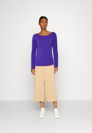 Purple long-sleeve top with a scoop neckline, paired with beige wide-leg pants, and white sneakers. Clean design with soft textures.