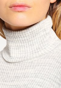 Hellgrauer Rollkragenpullover mit gerippter Textur. Verfügt über ein enganliegendes Design und weichen Stoff. Der Ausschnitt reicht bis zu einem hohen, strukturierten Kragen.