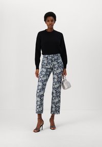 Pulover negru din tricot, pantaloni albaștri cu model floral, sandale negre cu toc și o geantă argintie. Design cu picior drept, cu accente florale vizibile.