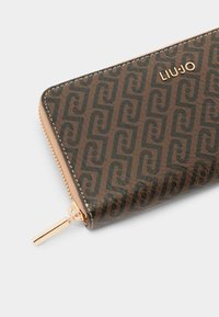 Portafoglio in pelle marrone con un motivo ripetuto, hardware color oro e chiusura a zip. Presenta un marchio impresso sulla superficie.