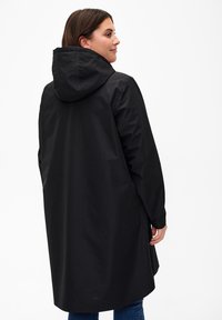 Svart vattentät kappa med huva, lång design, slät textur och sidofack för lätt rörelse. Har en minimalistisk stil.