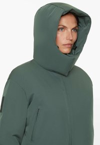 Green insulated jacket with a high collar and hood, featuring two side zippered pockets and a smooth, matte finish.