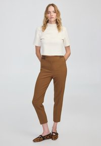 Cremfarbenes, kurzärmliges Crop-Top, braune tapered Hosen und schwarze Ballerinas mit einem Leopardenmuster. Glatte Stoffe, taillierte Passform.