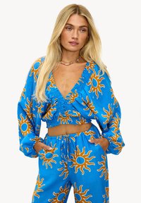 Tenue bleue composée d'un haut court à manches longues et d'un pantalon assorti, ornée de motifs de soleil orange. Tissu doux avec une coupe décontractée.