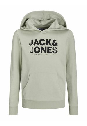 Personne portant un sweat à capuche vert clair avec le texte « "JACK & JONES" », un pantalon noir avec un logo sur la cuisse, et des baskets blanches avec des semelles noires.