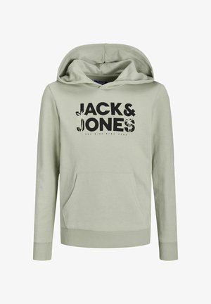 Personne portant un sweat à capuche vert clair avec le texte « "JACK & JONES" », un pantalon noir avec un logo sur la cuisse, et des baskets blanches avec des semelles noires.