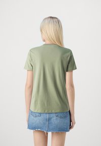 Olijfgroene katoenen t-shirt met korte mouwen en een ronde hals; heeft een rechte zoom en een gladde textuur. Draagt met een denimrok.