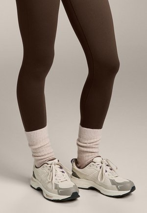 Bruna leggings, krämfärgade träningsskor med beiga accenter och lila detaljer, parat med ljusrosa ribbade strumpor.