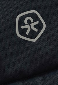 Sešstūru sudraba pieejamības ikona ar stilizētu cilvēka simbolu tumši pelēkā audumā ar smalku zāģēto zīmējumu.