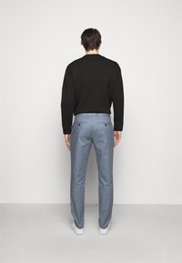 Černá mikina v kombinaci s světle modrými kalhotami. Kalhoty mají zadní kapsy se zapínáním na knoflíky. Model má na sobě bílé tenisky.