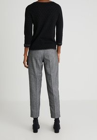 Maglione nero con maniche a tre quarti e motivo fine, abbinato a pantaloni a gamba affusolata grigi a quadri e stivaletti neri con tacco.