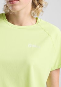 T-shirt verde chiaro a maniche corte realizzato in tessuto liscio, con colletto a girocollo e un piccolo logo bianco sul petto.
