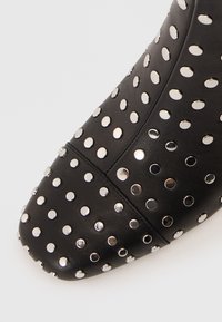 Black leather ankle boot with silver decorative studs, pointed toe, and smooth texture. Focus on stud pattern covering the upper.