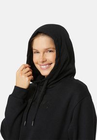 Black hooded sweatshirt with drawstring, textured fabric, and embossed logo. Features a relaxed fit and kangaroo pocket detail.
