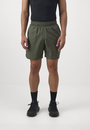 Mann trägt olivgrüne Shorts mit elastischem Bund, schwarzes ärmelloses Top, schwarze Socken und schwarze Schnürschuhe, steht vor einem schlichten Hintergrund.