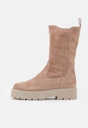 Botte mi-mollet en daim couleur fauve avec une semelle épaisse en caoutchouc beige et une languette à l’arrière, vue de profil sur fond blanc.