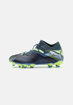 Voetbalschoenen met een marineblauwe bovenkant, voorzien van een textuurpatroon, groene accenten en spitse studschoenen voor grip.