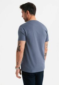 Camiseta de algodón gris con mangas cortas, cuello redondo y una textura suave. La parte posterior presenta un diseño minimalista sin logos ni patrones.
