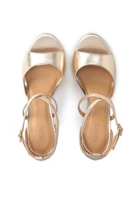 Kultaiset metalliset korkokenkä-sandaalit avonaisella varpaalla, ristiin menevällä remmillä ja soljella. Sileä pinta ja pehmustettu sisäpohja.