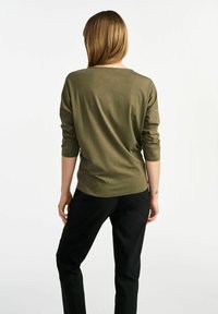 Oliwkowa bluzka z długim rękawem o luźnym kroju, ze okrągłym dekoltem i miękką fakturą, zestawiona z czarnymi spodniami, pokazana z tyłu.