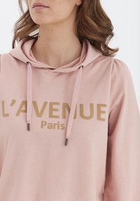 Ružová mikina s elastickým šnúrkou, s zlatým logom "L’AVENUE Paríž." Mäkký materiál, voľný strih a balónové rukávy.
