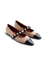 Scarpe flat beige con punte nere e cinturini neri decorati con grandi perle simili a perle lungo il dorso del piede, su uno sfondo bianco.