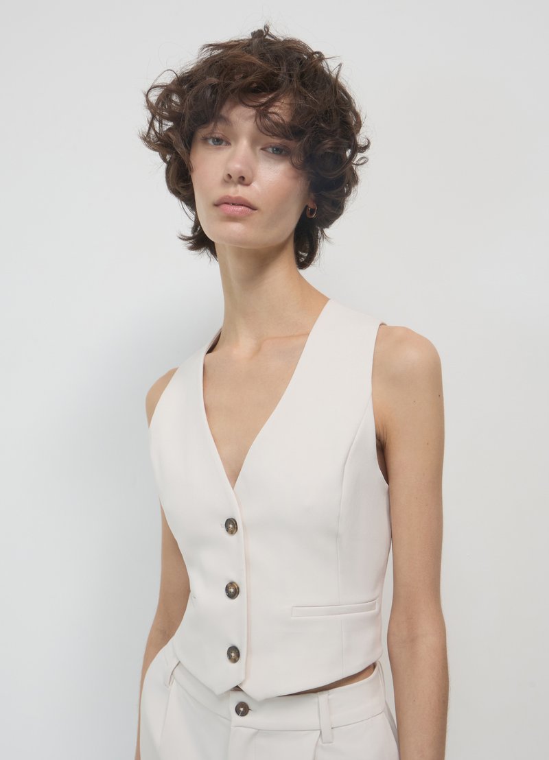 Gilet beige senza maniche con scollo a V profondo, cinque bottoni marroni e tasche laterali, realizzato in tessuto liscio, taglio curato.