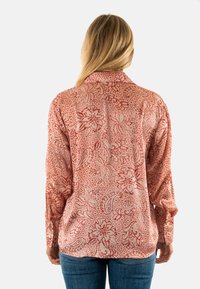 Camisa de patrón floral rojo con mangas largas, cuello y un ajuste ligeramente holgado. Fabricada en tejido ligero, con detalles intrincados.