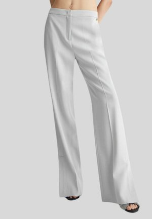 Pantaloni bianchi a gamba larga con una superficie liscia, dotati di zip frontale e chiusura con bottone. Accentuati da un dettaglio metallico in vita.