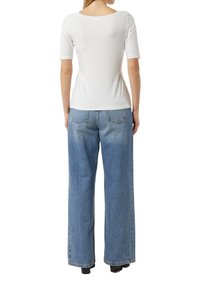 Biała bluzka z krótkim rękawem i szerokim dekoltem, zestawiona z jasnoniebieskimi jeansami o szerokich nogawkach, z tylnymi kieszeniami i luźnym krojem.