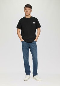 Czarna koszulka z krótkim rękawem z małym nadrukiem na klatce piersiowej, w połączeniu z niebieskimi dżinsami i białymi trampkami. Prosty i casualowy design.