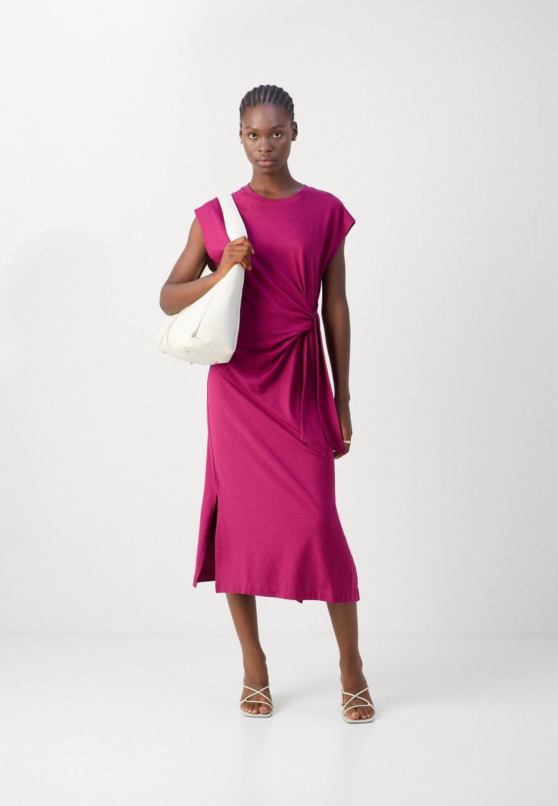 Fuchsia, knielanges Kleid mit geknotetem Taillendesign und kurzen Ärmeln. Kombiniert mit einer weißen, mondförmigen Tasche und Riemchensandalen.