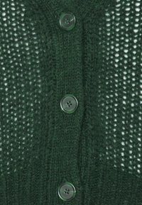 Grüne Strickjacke mit einem strukturierten Muster und großen, durchsichtigen Knöpfen vorne. Glattes Wollgewebe mit feiner Flaum.