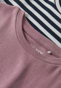 Close-up af en lyngfarvet rundhalset sweater lagdelt over en sort-hvid stribet stofbaggrund.